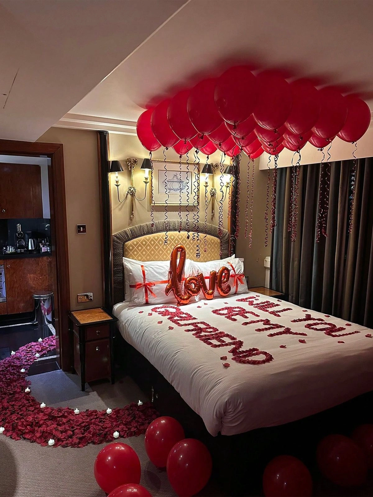 Romantic anniversary bedroom decoration with red ceiling balloons, rose petals spelling Happy Anniversary, LOVE balloon and candles