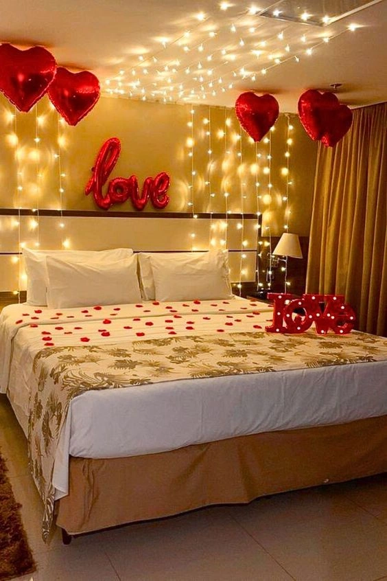 Romantic anniversary bedroom decoration with fairy lights, red heart balloons, LOVE sign and rose petals on the bed