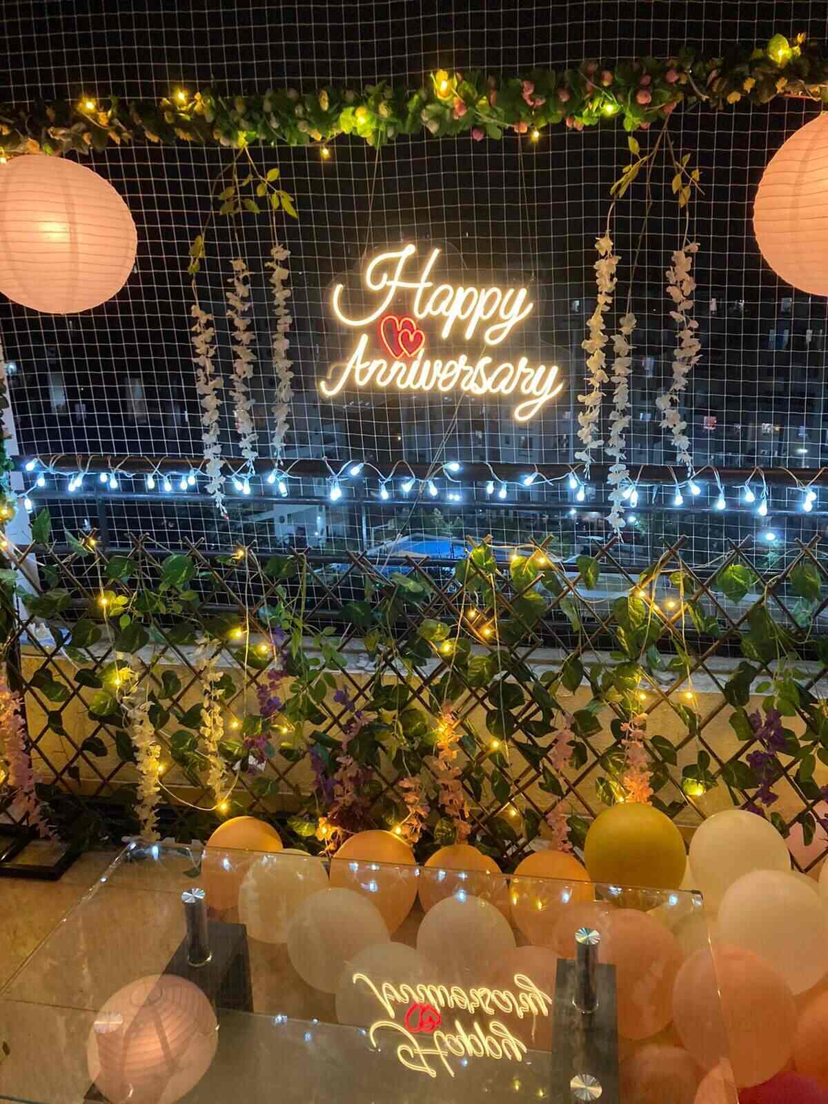 Outdoor anniversary decoration with fairy lights, greenery, hanging florals and Happy Anniversary neon sign