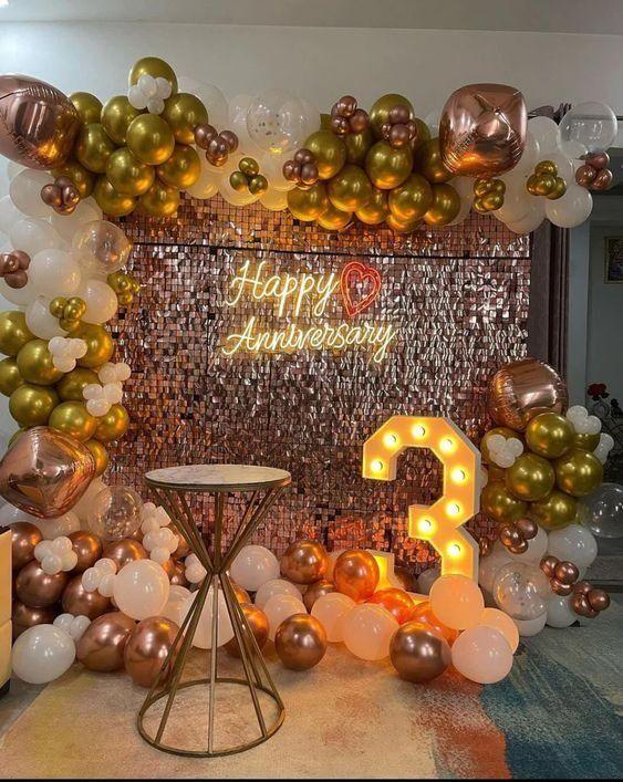 Rose gold, white and gold anniversary decoration with sequin backdrop, balloon arch, Happy Anniversary neon sign and illuminated number 3