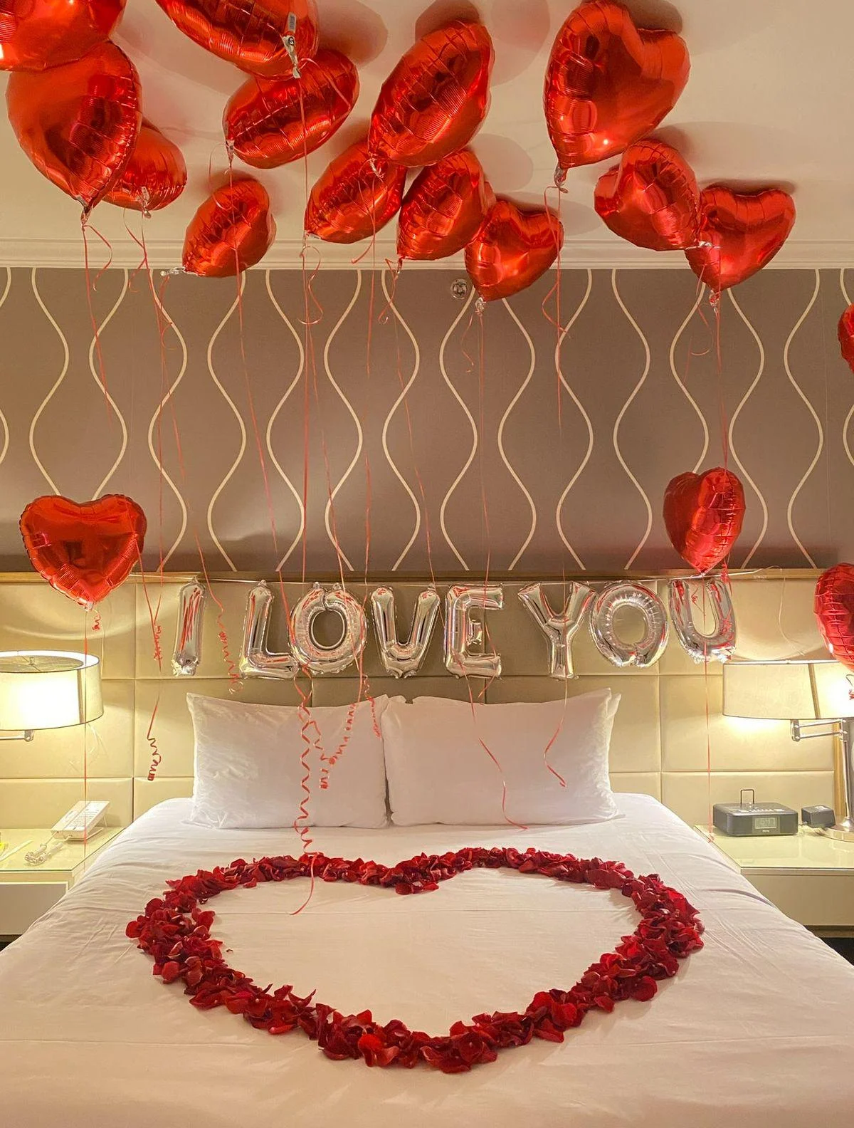 Romantic hotel room anniversary decoration with red heart balloons, I LOVE YOU foil letters and rose petal heart