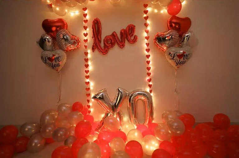 Romantic anniversary wall decoration with LOVE and XO foil balloons, heart balloons, fairy lights and red floor balloons