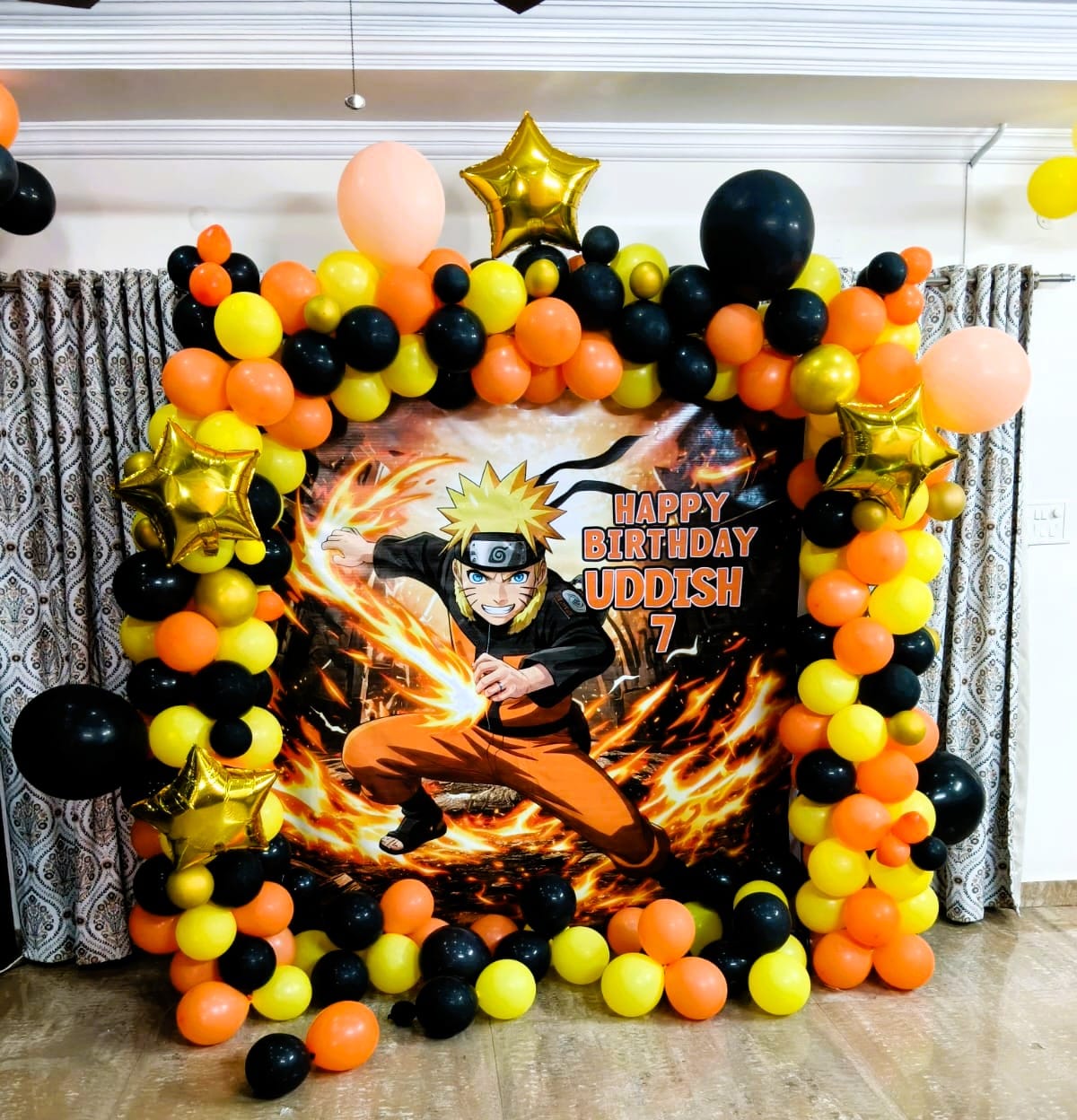 Naruto-themed birthday decoration with orange, yellow and black balloons and gold star balloons