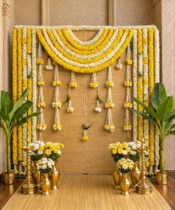 Alternative woven puja backdrop with yellow-and-white garlands, banana plants, brass lamps and flower-filled vases