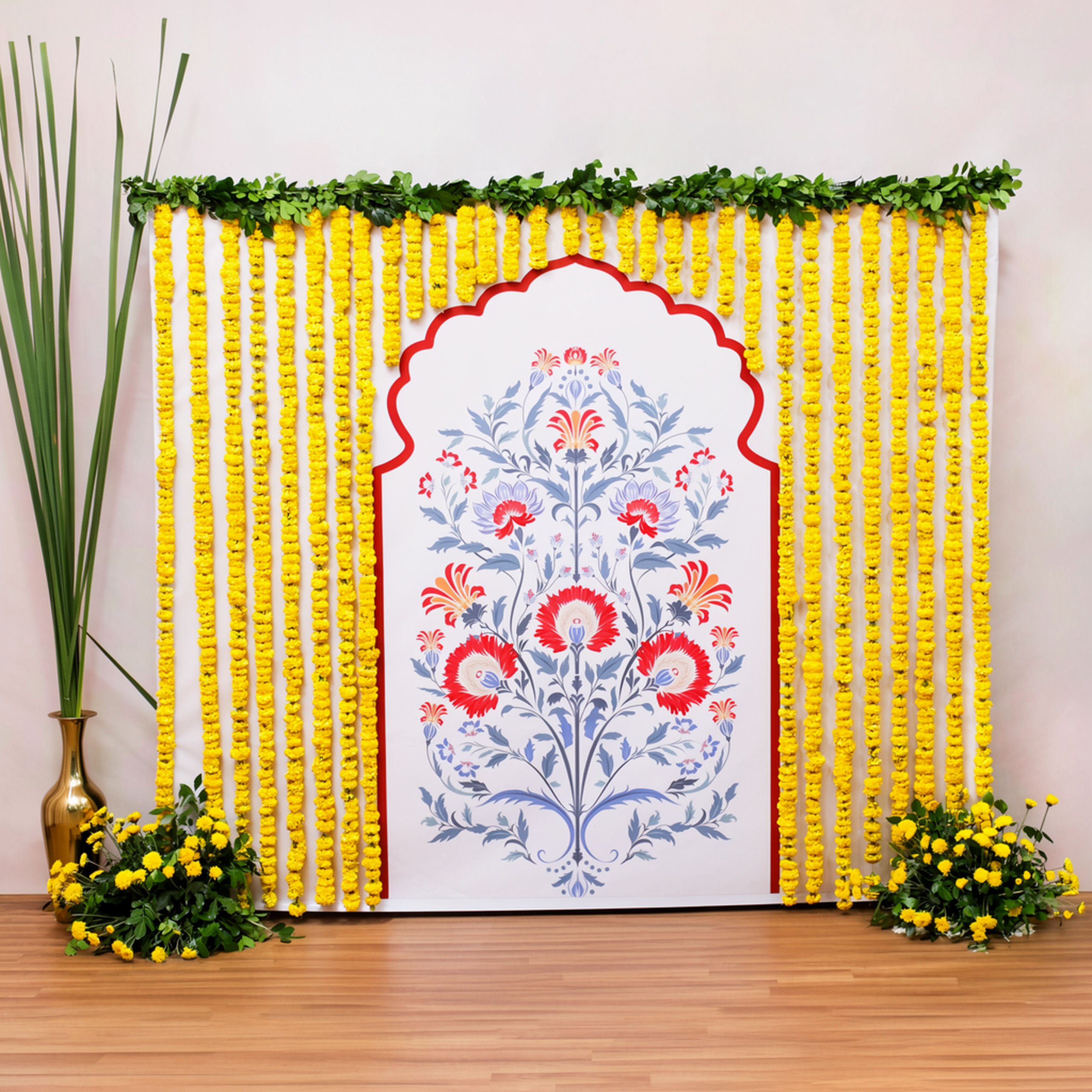 Printed floral puja backdrop framed by yellow marigold strings with two floor bouquets and an additional tall golden pot with grass
