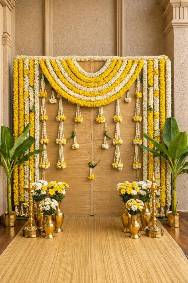 Alternative woven puja backdrop with yellow-and-white garlands, banana plants, brass lamps and flower-filled vases