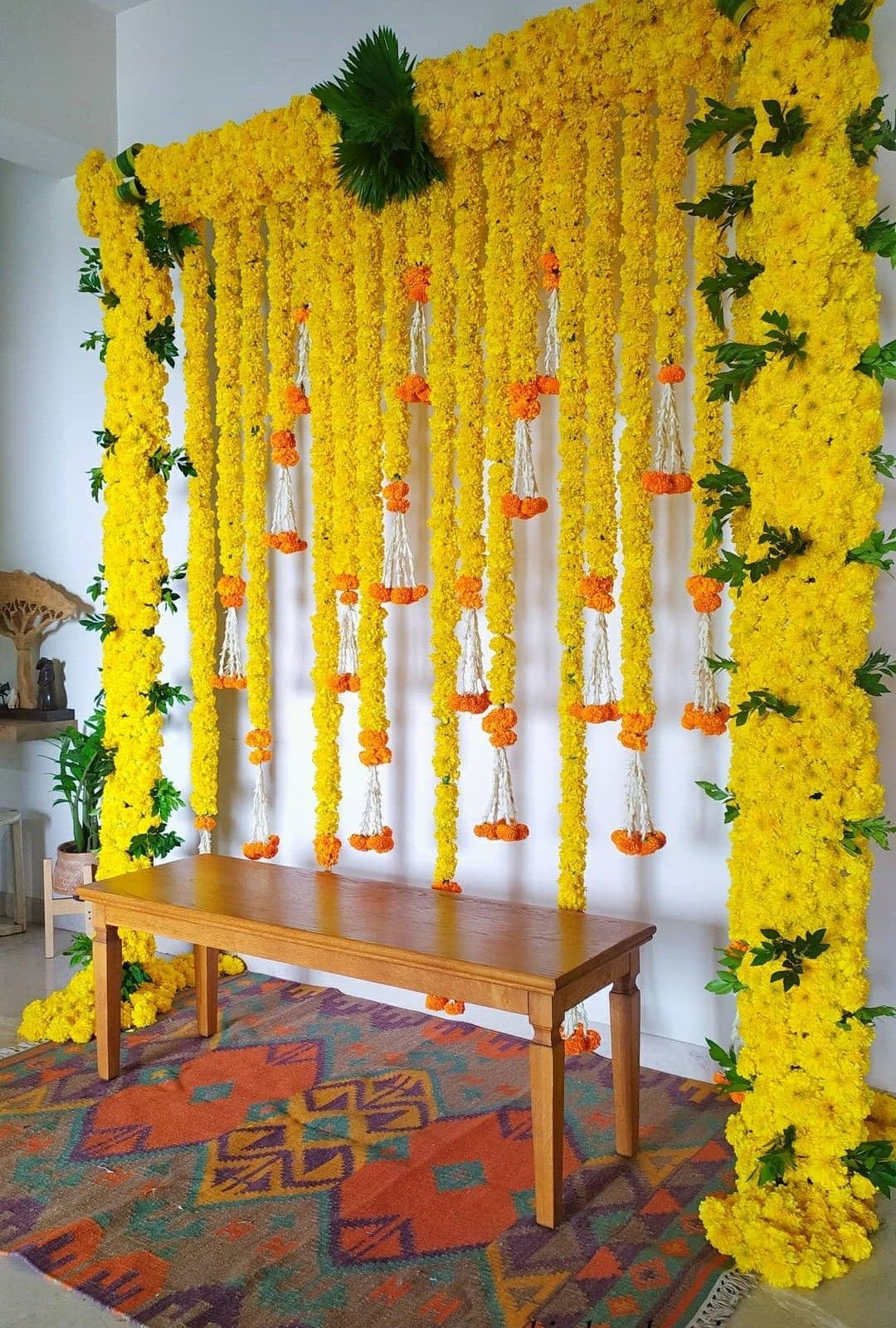 Alternative yellow floral backdrop with green foliage and orange-and-white hanging accents behind a wooden table