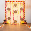 Pink and yellow Diwali backdrop with triangular tassels, patterned rangoli hangings, decorated pots and additional floor rangoli with LED candles