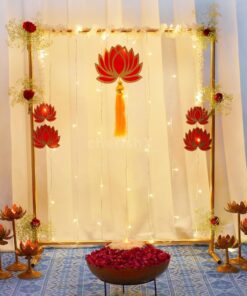 Alternative gold-frame puja backdrop with red lotus cutouts, fairy lights, lotus candle stands and a flower-filled bowl