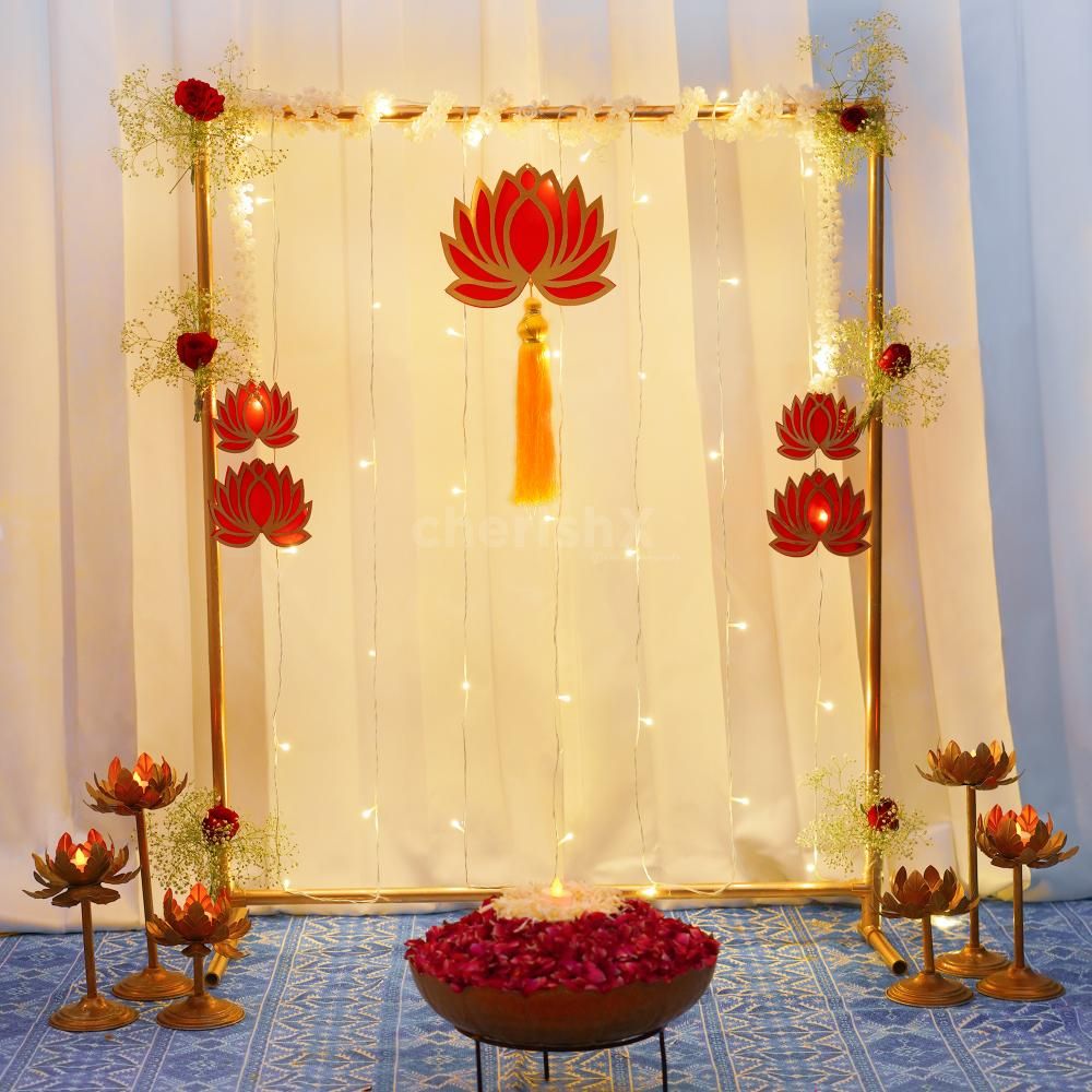 Alternative gold-frame puja backdrop with red lotus cutouts, fairy lights, lotus candle stands and a flower-filled bowl