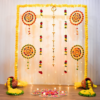 Yellow garland Diwali backdrop with a central diya hanging, four colourful circular accents, decorated pots and additional floor rangoli with LED candles