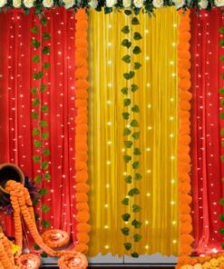 Alternative red and yellow draped backdrop with fairy lights, green leaf strings, floral trim and decorative floor styling